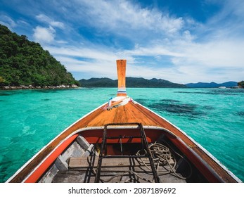 Scenic view from wooden long tail boat prow on crystal clear turquoise sea water bay with coral reef against summer blue sky. Near Koh Lipe Island, Tarutao National Marine Park, Satun, Thailand.
