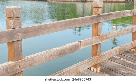 A scenic view of a wooden railing along a dock with calm water in the background. Ideal for themes related to outdoor structures, nature, and serene landscapes - Powered by Shutterstock