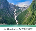 Scenic waterfall, partly frozen, with meltwater from icy mountaintop along Tracy Arm fjord on a sunny morning early in summer in southeast Alaska