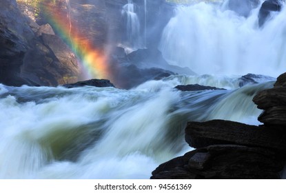 Scenic Waterfall With Rainbow In Background.