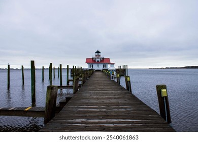 Scenic waterfront photo featuring a wooden pier leading to a quaint lighthouse with a red roof under an overcast sky.  - Powered by Shutterstock