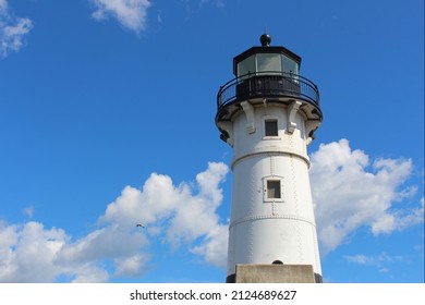 Scenic white and black lighthouse with blue sky and white clouds.