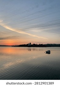 Scenic Wide Angle View Of Small Boat Anchored On Calm Water At Sunset With Cargo Ship In Background Under Colorful Evening Sky