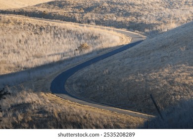 Scenic winding road cutting through dry, rolling hills. The minimalist landscape captures the natural beauty of remote, hilly terrain under soft sunlight. - Powered by Shutterstock