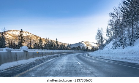 Scenic Winter Dangerous Icy Slippery Winding Highway Road With Piles Of Snow On The Side Of The Road After Clearing The Road And Snow-covered Mountains Overgrown With Spruce Forest In Montana