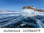 Scenic winter landscape of frozen Baikal Lake on sunny cold day. View of Cape Kobylya Golova or Mare Head of Olkhon Island with thick crust. Smooth surface of transparent ice with cracks and bubbles