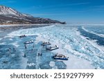 A scenic winter landscape of people walking and exploring a frozen lake surrounded by snow-covered mountains. Hovercrafts and groups of adventurers stand on the transparent ice. Lake Baikal in winter.