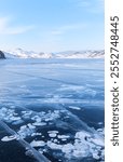 Scenic winter landscape with white gas bubbles on blue clear ice surface on frozen Baikal Lake on cold winter sunny day. Snow-covered white mountains and hills on distance. Winter natural background