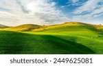 sceniv view at a nice farm in green fields in hills and highlands, landscape of spring green hills with mountain bright sunset on backdrop