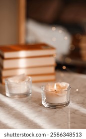 Scented burning candle with stack of paper books on marble table in room close up.