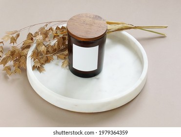Scented Candle In A Glass Jar Mockup On A Marble Tray And Dry Grass Plant On Beige Background. Copy Space