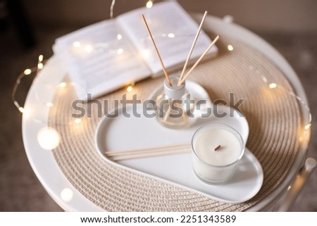 Scented candle with liquid home fragrance on tray at coffee table on knit cloth textile. Cozy atmosphere. 