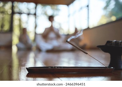 Scented stick on a wooden stand holder. Burning aromatic incense smoky stick with meditating people group doing yoga on background. Aromatherapy smoke for yoga and meditation healing practices concept - Powered by Shutterstock