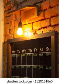 Schedule Black Board On A Brick Wall Under Lighten Bulb Lamp. Week Days Boxes To Write Down Dates, Timings Or Events By Piece Of Chalk. Old School Style Interior Design