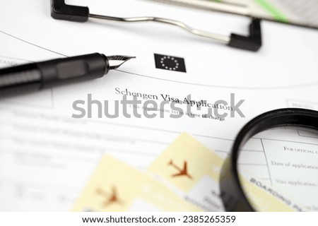 Schengen visa application on A4 tablet lies on office table with pen and magnifying glass close up