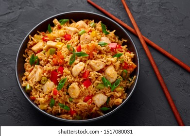 Schezwan Chicken Fried Rice in black bowl at dark slate background. Szechuan Rice is indo-chinese cuisine dish with bell peppers, green beans, carrot, chicken breasts.