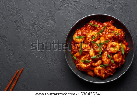 Schezwan Prawns in black bowl at dark slate background. Schezwan Prawns is indo-chinese cuisine curry dish with prawns or shrimps roasted in Schezwan Sauce. Foto d'archivio © 