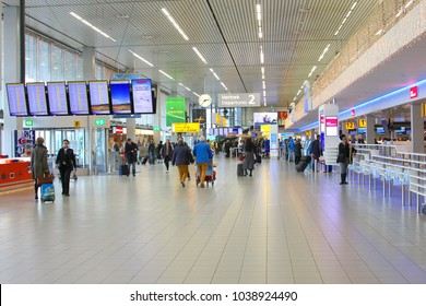 SCHIPHOL AMSTERDAM AIRPORT, NETHERLANDS - January 9, 2018. Elderly couple and younger travellers are walking with luggage trolleys at KLM self  service check in desks in departure hall of terminal 2.