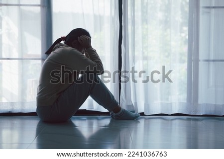 Schizophrenia with lonely and sad in mental health depression concept. Depressed woman sitting against floor at home with dark room feeling miserable. Women are depressed, fearful and unhappy.