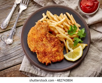 schnitzel and fried potatoes on dark plate, top view