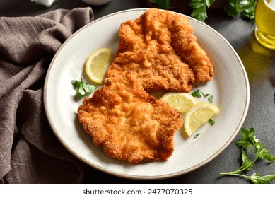 Schnitzel with lemon and leaves of parsley on white plate over brown stone background.  Close up view