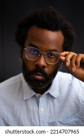 Scholarly Looking Black Man With A Salt And Pepper Beard Posing With Stylish Gold Wire Frame Glasses And Light Blue Shirt Looking Directly Into The Camera