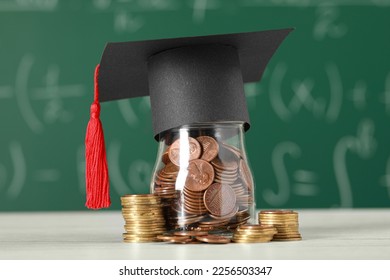 Scholarship concept. Glass jar with coins and graduation cap on white wooden table