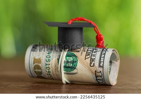 Scholarship concept. Graduation cap and dollar banknotes on wooden table, closeup