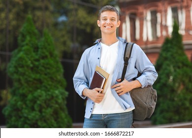 Scholarship Grant. Portrait Of Happy College Student Guy With Backpack And Books Over University Campus Background, Selective Focus