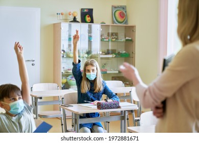 Schoo children with hands raised in classroom during a pandemic - Shutterstock ID 1972881671