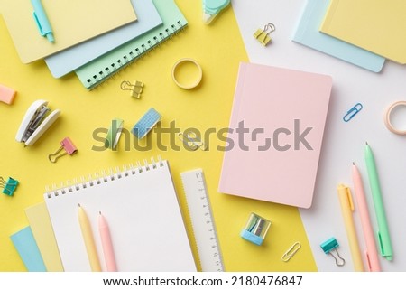 School accessories concept. Top view photo of colorful notebooks sharpener ruler corrector pens binder clips adhesive tape and stapler on bicolor yellow and white background