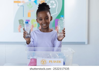 In school, african american girl holding plastic bottles and recycling in classroom. environment, sustainability, education, waste management, eco-friendly, awareness - Powered by Shutterstock