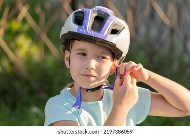 School Age Biker, Child Taking Off Or Putting On A Protective Biking Helmet, Young Cyclist Portrait, Face Closeup, Girl Fastening Her Helmet. Blurred Background, Children And Biking, Cycling, Sports