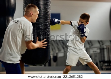 School age boy, beginner boxer practicing punches with personal coach at sports gym, indoors. Concept of studying, challenges, sport, hobbies, competition. Beginning of sports career, future champion