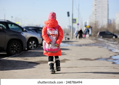 School aged kid girl with backpack walking on the sidewalk after school in sunny spring day