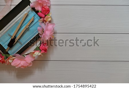 School or back to school concept: divider, blue medical mask (protective mask), dark notebook and pink floral wreath on a wood background 