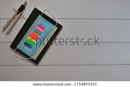 School or back to school concept: divider, multicolored sticky notes, blue medical mask (protective mask) and dark notebook on a wood background