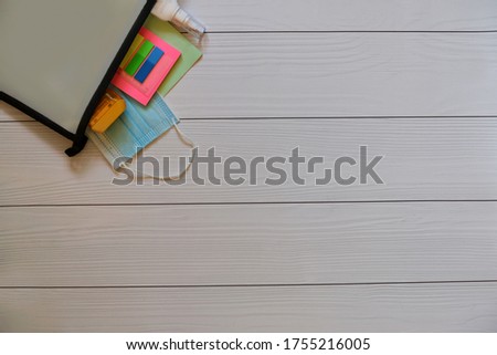 School or back to school concept: folder for notebooks with multicolored sticky notes, yellow sharpener, blue medical mask (protective mask), green exercise book on a wood background