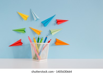School background with colorful pencils and paper planes against blue wall. Copy space. - Shutterstock ID 1405630664