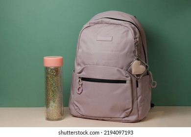 A School Backpack With A Bottle Of Water On A Table On A Green Background. Preparation For School. High Quality Photo