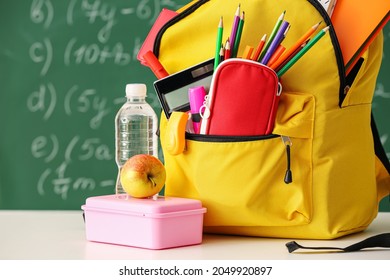 School Backpack With Stationery, Bottle Of Water And Lunchbox On Table In Classroom, Closeup