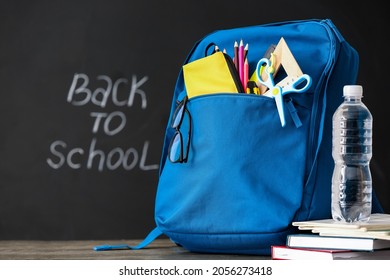 School Backpack With Stationery, Eyeglasses And Bottle Of Water On Table In Classroom