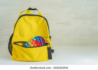 School Bag With Sensory Fidget Toys Inside On White Wooden Background With Copy Space. Back To School Concept. Antistress Concept.