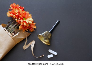 School bell and chalk on blackboard with flowers teacher day abstract background