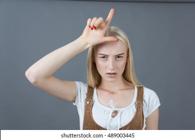 School blonde girl showing loser sign studio gray background