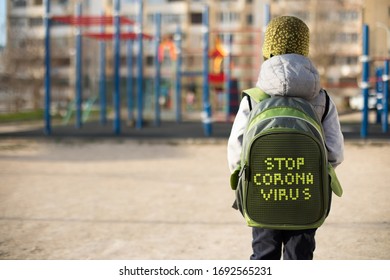 A School Boy With A Backpack With Inscription Stop Coronavirus In Front Of The Empty Playground During Coronavirus Quarantine. Social Distance, Self-isolation Concept.