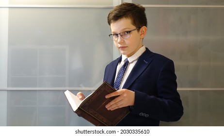 School boy in eyegasses and school uniform is holding a book. Wardrobe background.