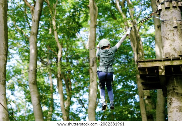 School boy in forest adventure park. Acitve
child, kid in helmet climbs on high rope trail. Agility skills and
climbing outdoor amusement center for children. Outdoors activity
for kid and families.