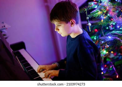 School Boy With Glasses Playing Piano In Living Room. Child Having Fun With Learning To Play Music Instrument. Talented Kid With Christmas Tree On Background. Family Xmas Celebration.