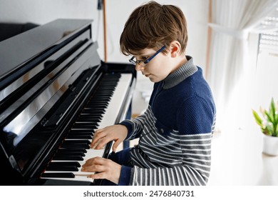 School boy with glasses playing piano in living room. Child having fun with learning to play music instrument. Talented kid during homeschooling corona virus lockdown. - Powered by Shutterstock